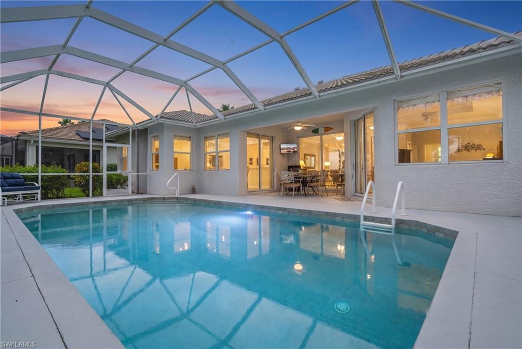 Screened-in swimming pool with a tiled perimeter, integrated lighting, and direct access to an outdoor patio featuring a ceiling fan and sliding glass doors