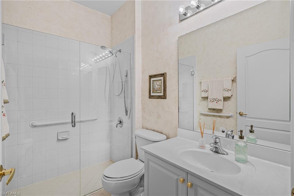 Glass-enclosed shower with white tiled walls, single vanity with integrated sink, chrome faucet, and overhead bar lighting