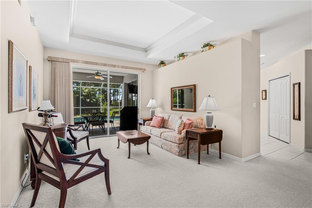 Tray ceiling accentuates the living space, featuring neutral carpeting and a half-wall partition