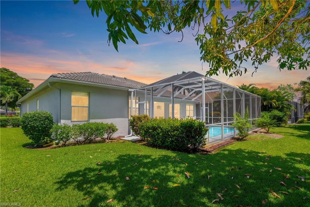 Screened-in swimming pool enclosure, stucco exterior, tile roof, and manicured landscaping, set on a verdant lawn