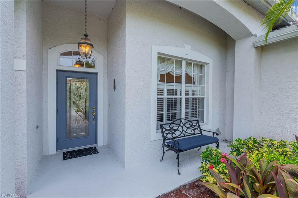 Recessed entryway featuring an arched transom window above a decorative glass door, a hanging lantern fixture, and a window with plantation shutters