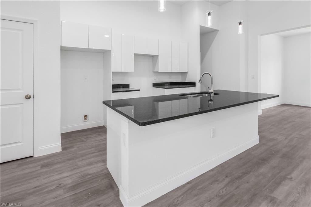 Kitchen with white cabinetry, dark stone countertops, dark wood finished floors, a high ceiling, and a center island with sink
