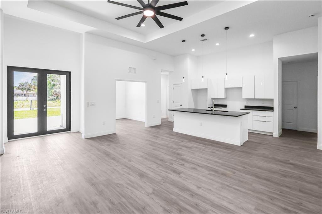 Kitchen with a high ceiling, dark countertops, white cabinetry, an island with sink, and open floor plan