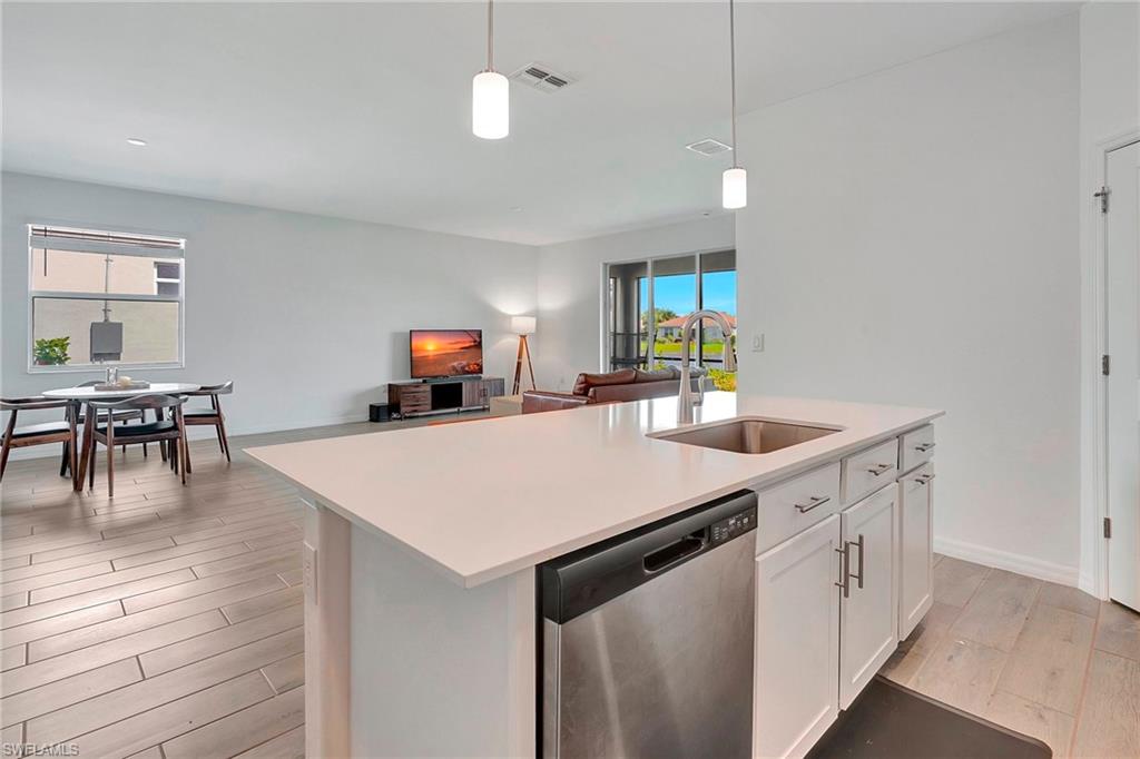 Kitchen featuring dishwasher, light hardwood / wood-style floors, sink, a kitchen island with sink, and white cabinets