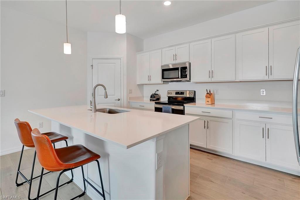 Kitchen featuring appliances with stainless steel finishes, light hardwood / wood-style floors, white cabinetry, sink, and a kitchen island with sink