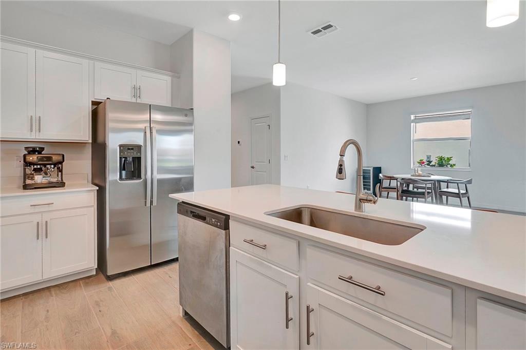 Kitchen featuring appliances with stainless steel finishes, light hardwood / wood-style flooring, sink, pendant lighting, and white cabinets