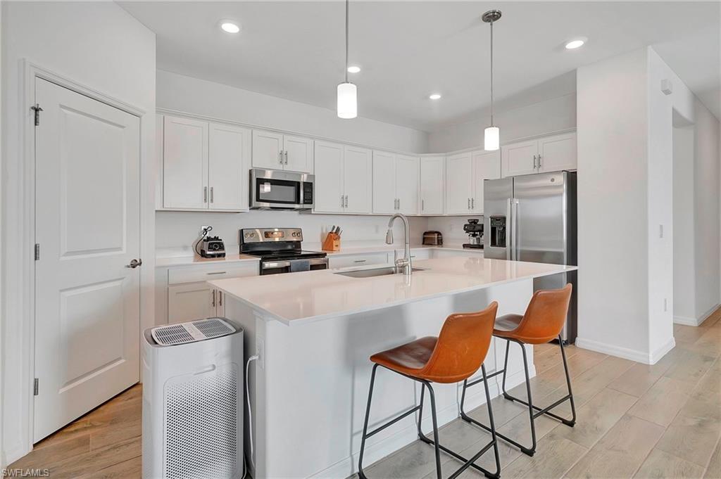 Kitchen with light wood-type flooring, an island with sink, white cabinetry, sink, and stainless steel appliances