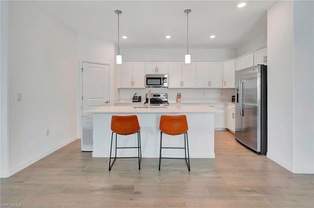 Kitchen with appliances with stainless steel finishes, decorative light fixtures, an island with sink, and light wood-type flooring