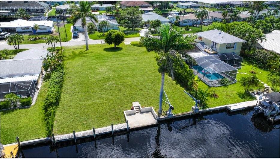Expansive green lawn with canal frontage, featuring a concrete dock and boat lift