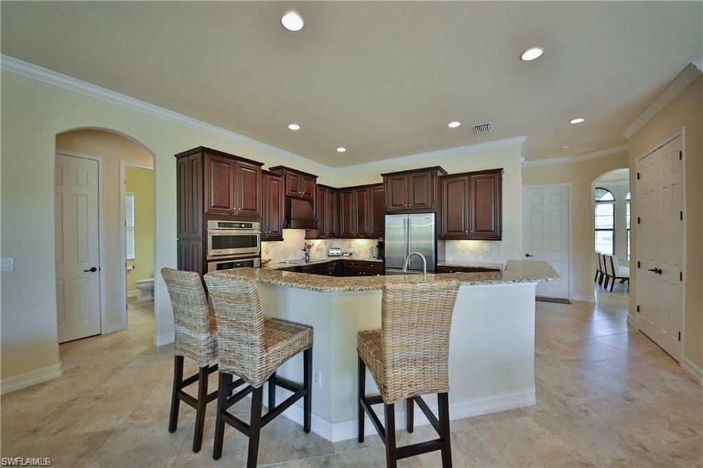 Kitchen with a large island, appliances with stainless steel finishes, light stone counters, a kitchen bar, and decorative backsplash