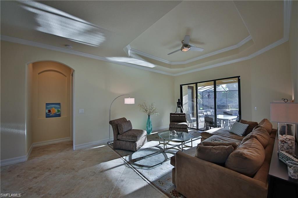 Living room with light tile patterned floors, ornamental molding, a raised ceiling, and ceiling fan