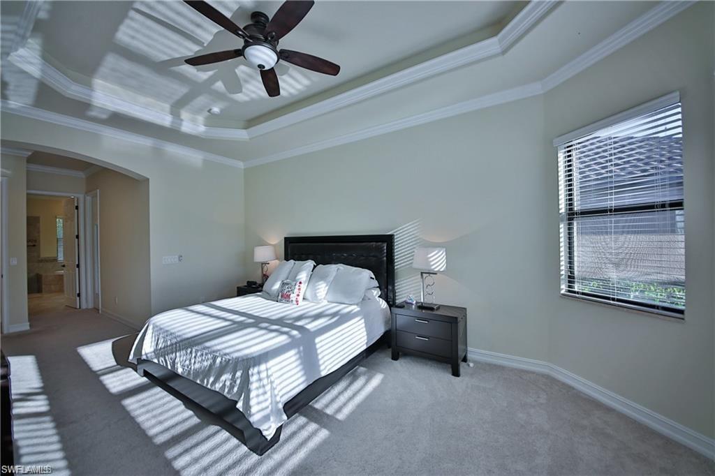 Carpeted bedroom featuring a tray ceiling, ornamental molding, and ceiling fan