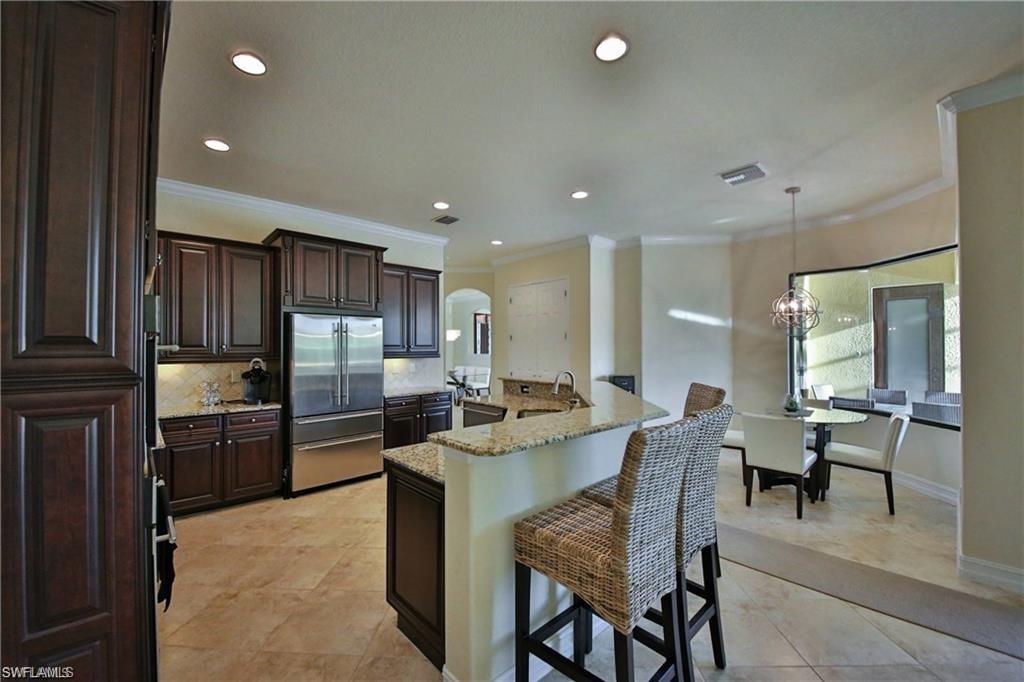Kitchen with high end fridge, ornamental molding, pendant lighting, light stone countertops, and decorative backsplash