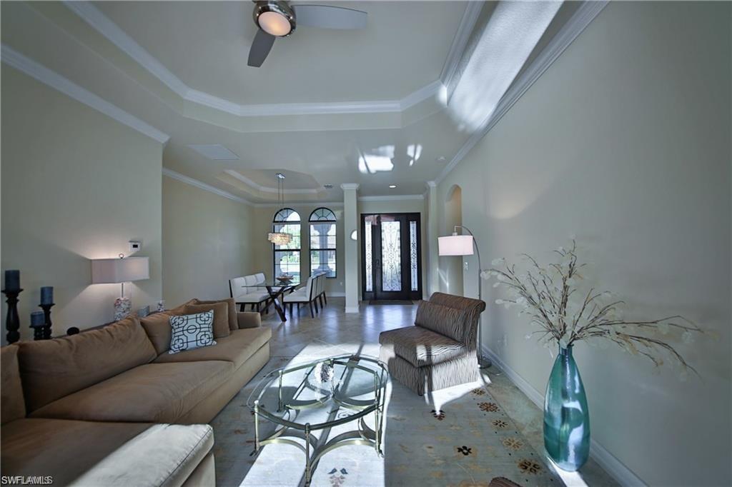 Tiled living room with ceiling fan, ornamental molding, a tray ceiling, and ornate columns