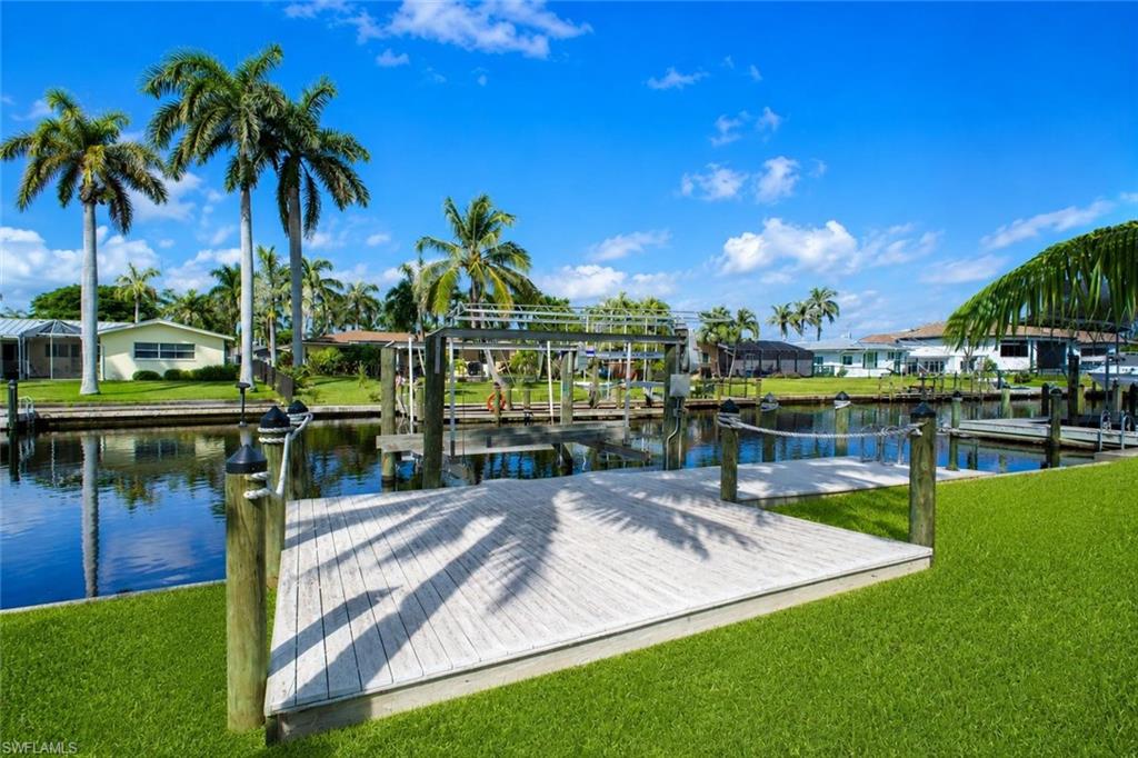 Renderd photo - Waterfront property featuring a wood dock, boat lift, and manicured lawn