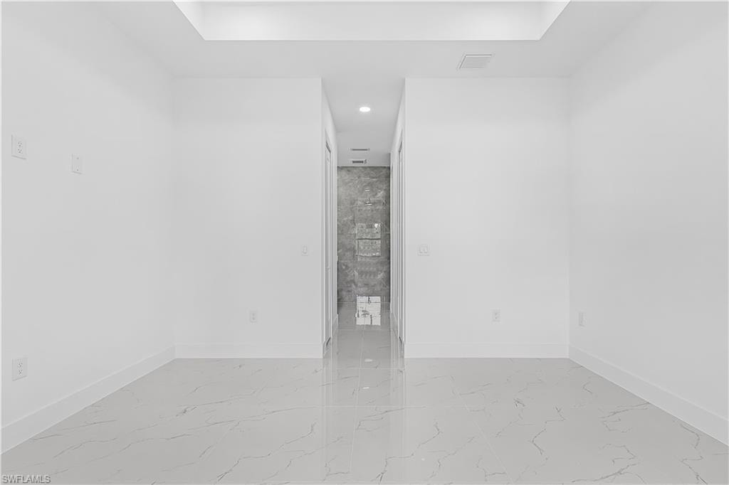 Recessed lighting, tray ceiling detail, light-toned walls, large format tile flooring, and a hallway with wall tiling