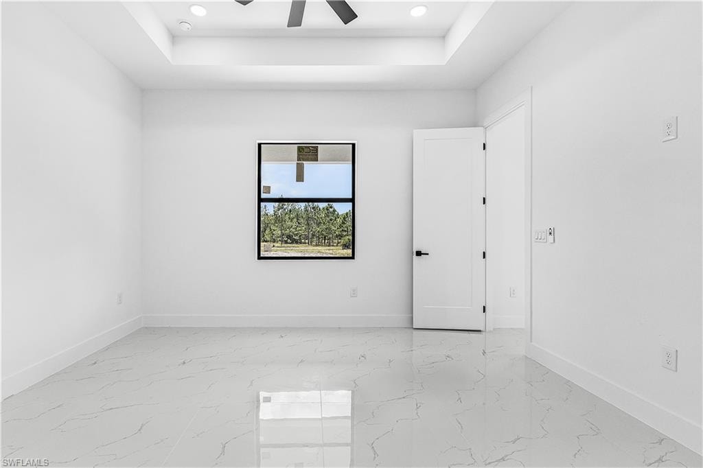 Recessed lighting, tray ceiling, ceiling fan, white paneled doors, and large-format tile flooring