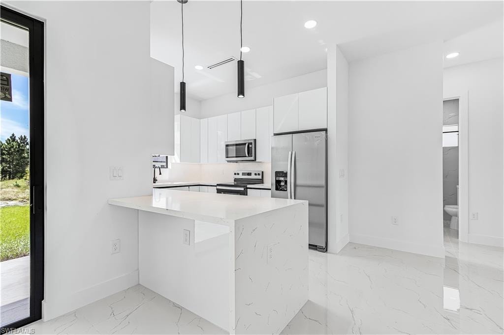 Modern kitchen featuring white cabinetry, stainless steel appliances, a breakfast bar with a solid surface countertop, and pendant lighting