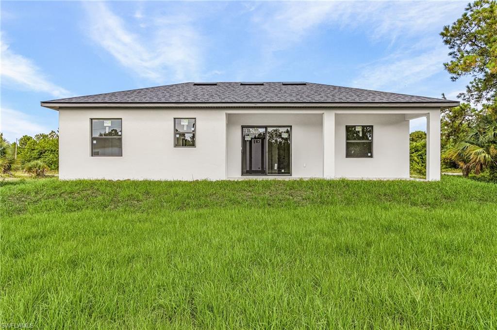 Rear exterior featuring a covered patio, sliding glass doors, white stucco finish, and a dark shingle roof