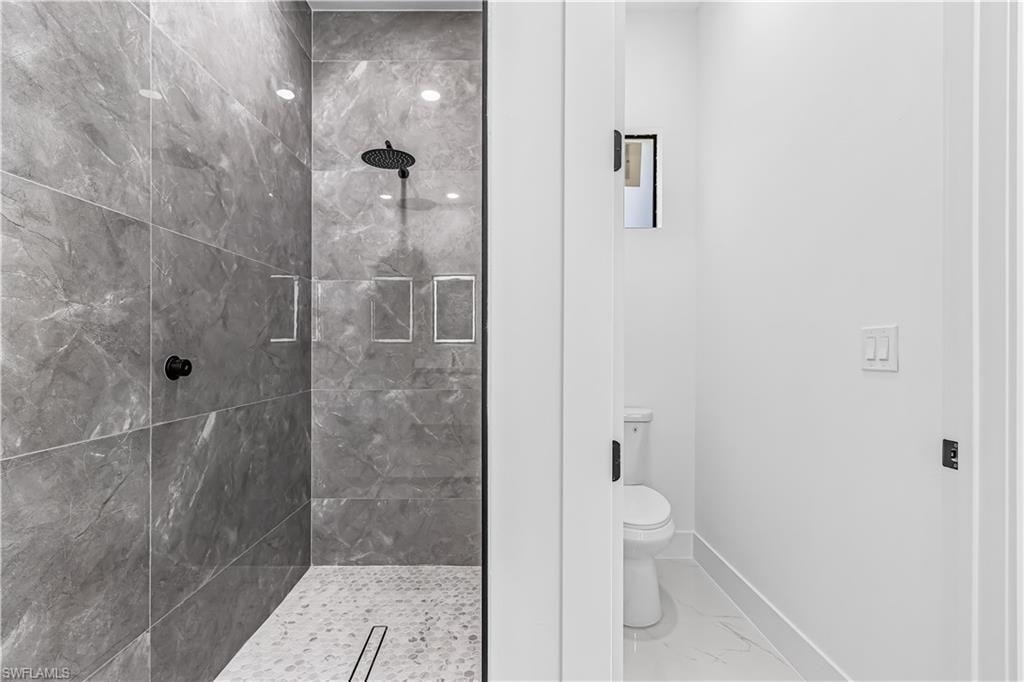 Glass-enclosed shower with large format gray wall tile, rainfall showerhead, and recessed niche shelving