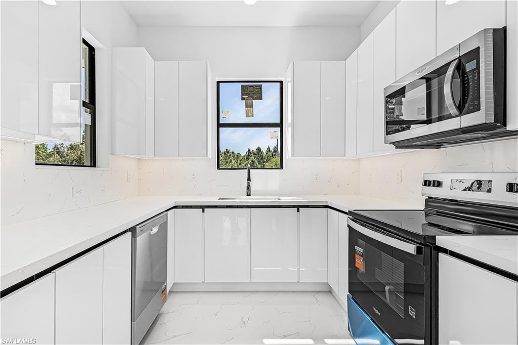 U-shaped kitchen with white gloss cabinetry, white countertops, stainless steel appliances, and a white backsplash