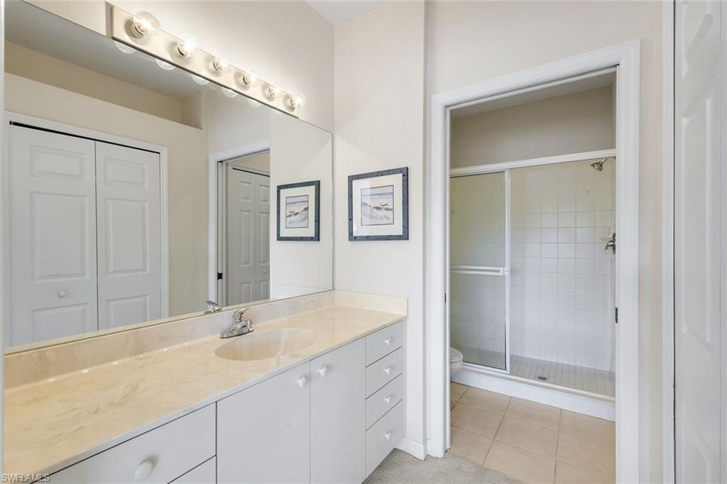 Primary Bathroom Featuring a White Vanity with a Light-Toned Countertop, Large Mirror, Pocket Door to the Private Water Closet and Walk-In Shower, and Spacious Walk-In Closet