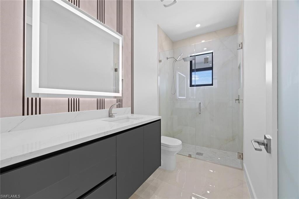 Vanity with integrated sink and chrome faucet, back-lit mirror, glass-enclosed shower, wall-mounted showerhead, and window
