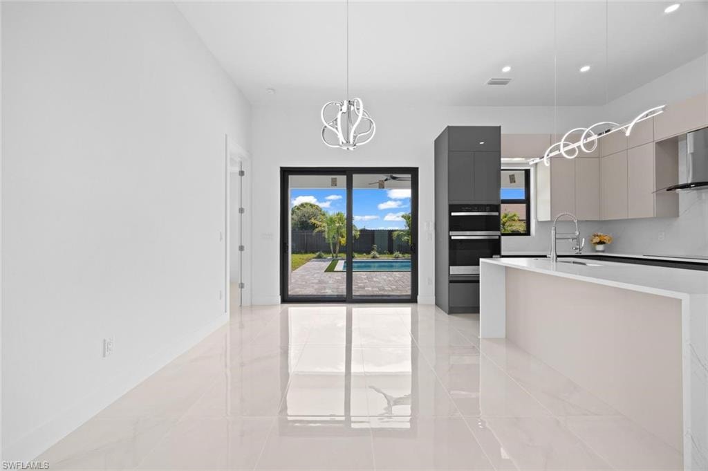 Polished tile flooring, modern pendant lighting, kitchen island with sink, built-in double ovens, and sliding glass doors opening to an outdoor pool