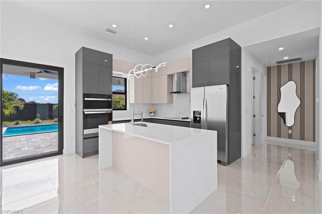 Gleaming polished tile flooring, contemporary kitchen with built-in stainless steel appliances, large center island with integrated sink, sliding glass door leading to a pavered patio and pool