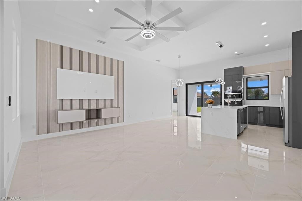 Expansive open-concept living area featuring large format tile flooring, a vaulted ceiling with a contemporary ceiling fan, and a built-in media console