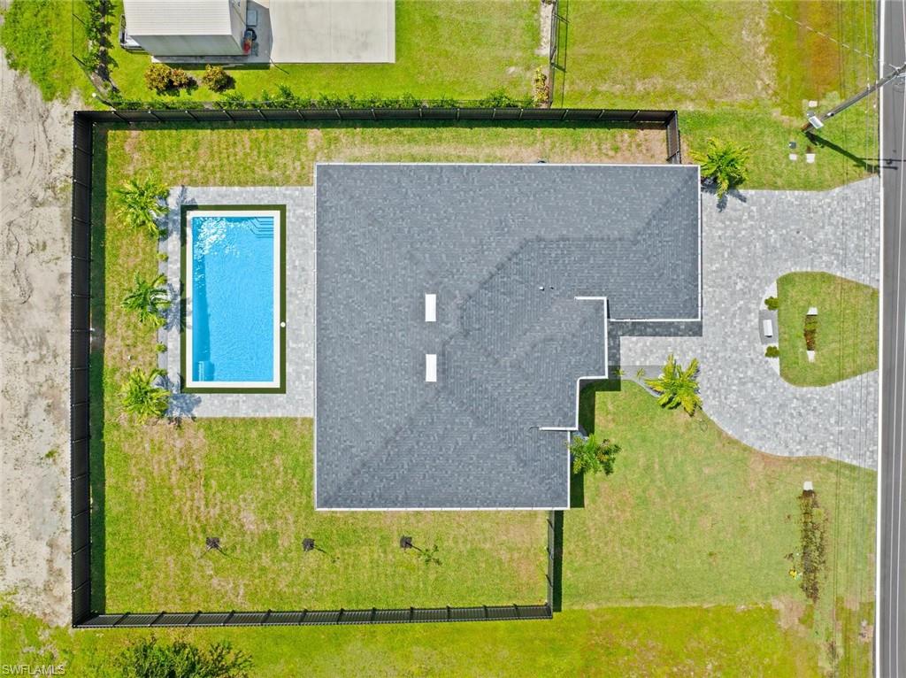 Rectangular swimming pool with paved surround, expansive green lawn, and a paved driveway