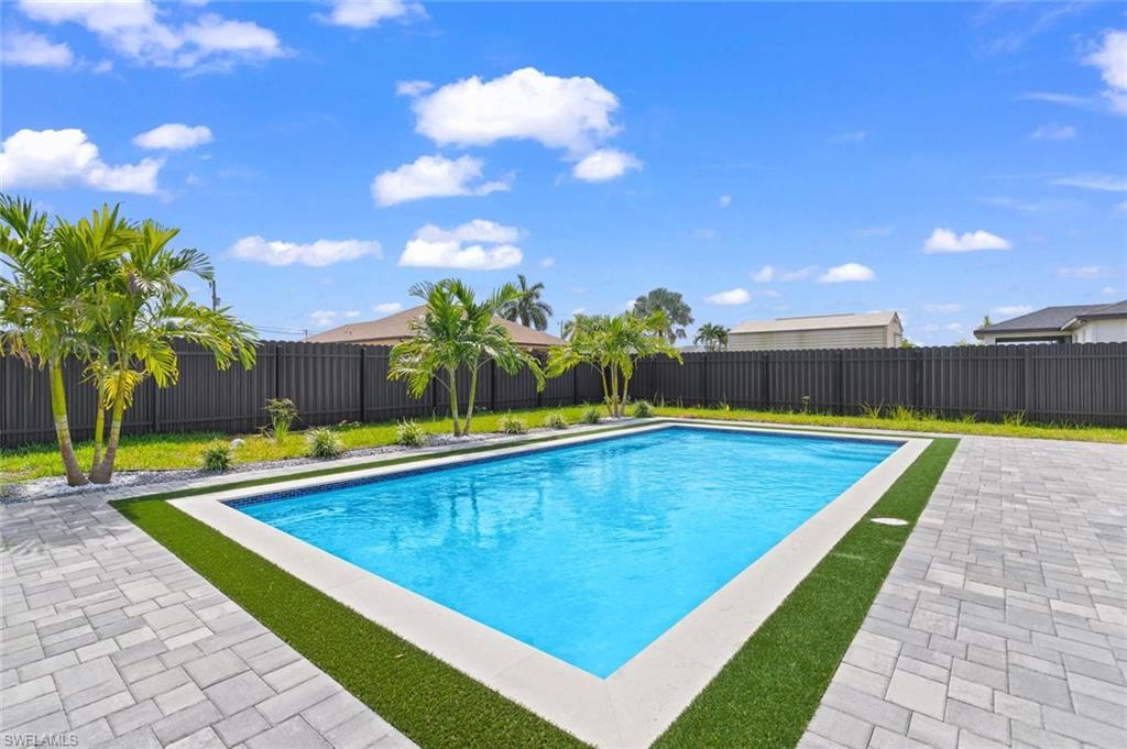 Outdoor swimming pool with paver decking, artificial turf accents, and perimeter landscaping