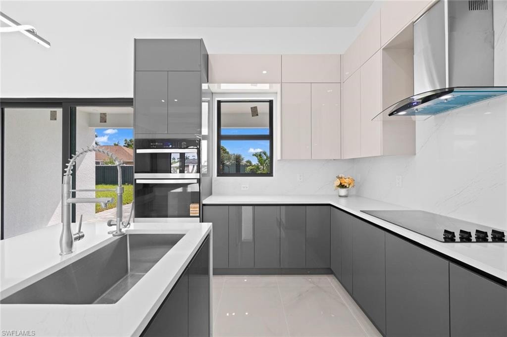 Modern kitchen featuring white countertops, an undermount sink, built-in stainless steel appliances, and two-tone high-gloss cabinetry