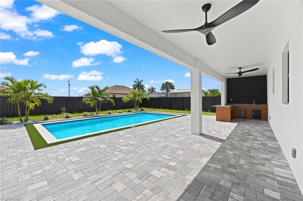 Expansive paved patio with a rectangular swimming pool, outdoor kitchen, and two ceiling fans