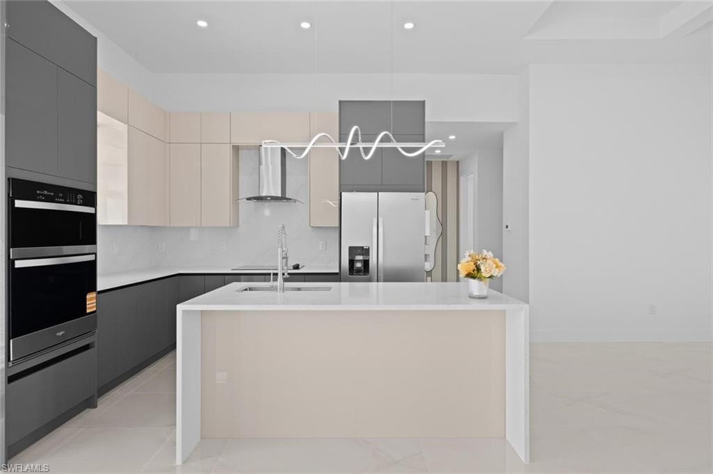 Contemporary kitchen featuring two-tone cabinetry, a waterfall island with a light-toned panel, stainless steel double wall ovens, and a matching refrigerator