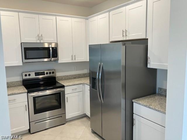 Kitchen featuring light tile patterned floors, stainless steel appliances, light stone counters, and white cabinetry