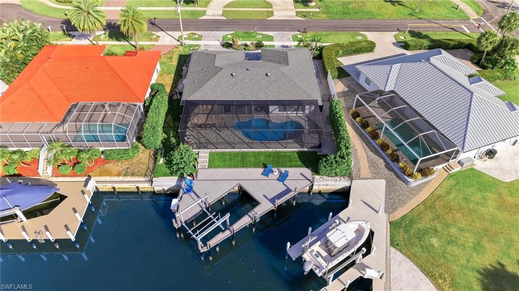 Screened pool enclosure with a freeform pool, mature landscaping, and a waterfront dock with boat lifts