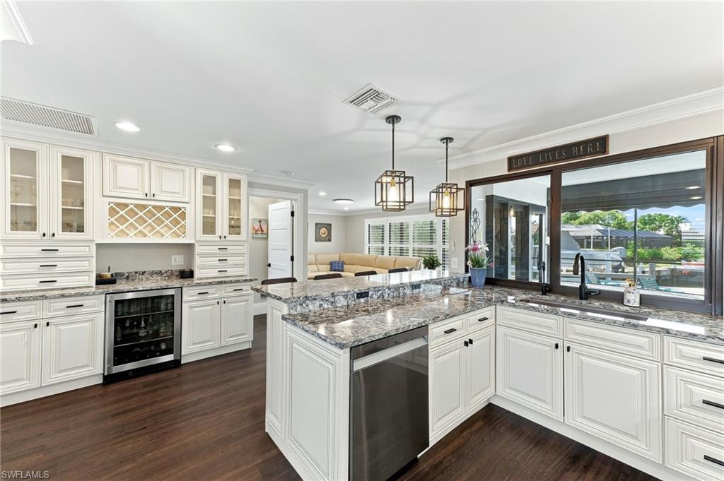 White shaker cabinetry, patterned stone countertops, stainless steel appliances, dark wood-finish flooring, and a built-in wine rack