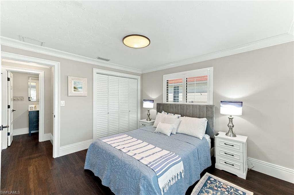 Dark wood-finish flooring, crown molding, and white louvered closet doors