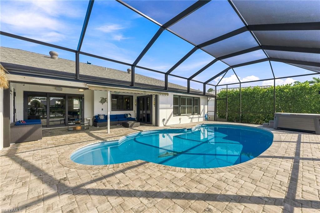 Screened-in pool deck featuring a freeform pool, integrated spa, and extensive paver patio