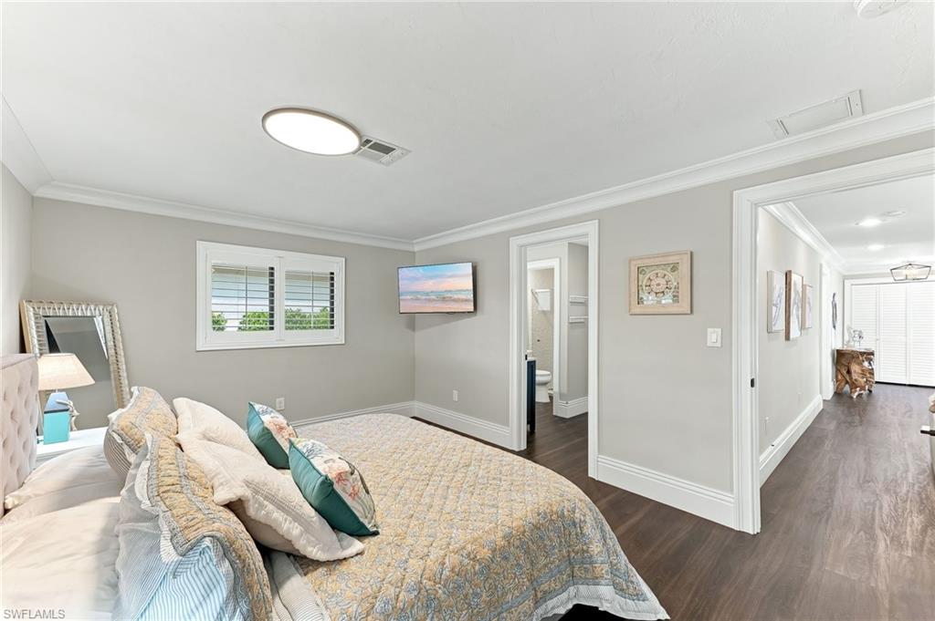 Spacious room featuring plantation shutters, crown molding, and dark wood-finish flooring