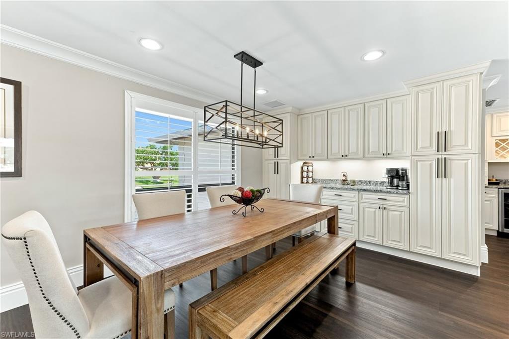Wood-finish flooring, white shaker-style cabinetry, dark stone countertops, recessed lighting, and a contemporary linear chandelier