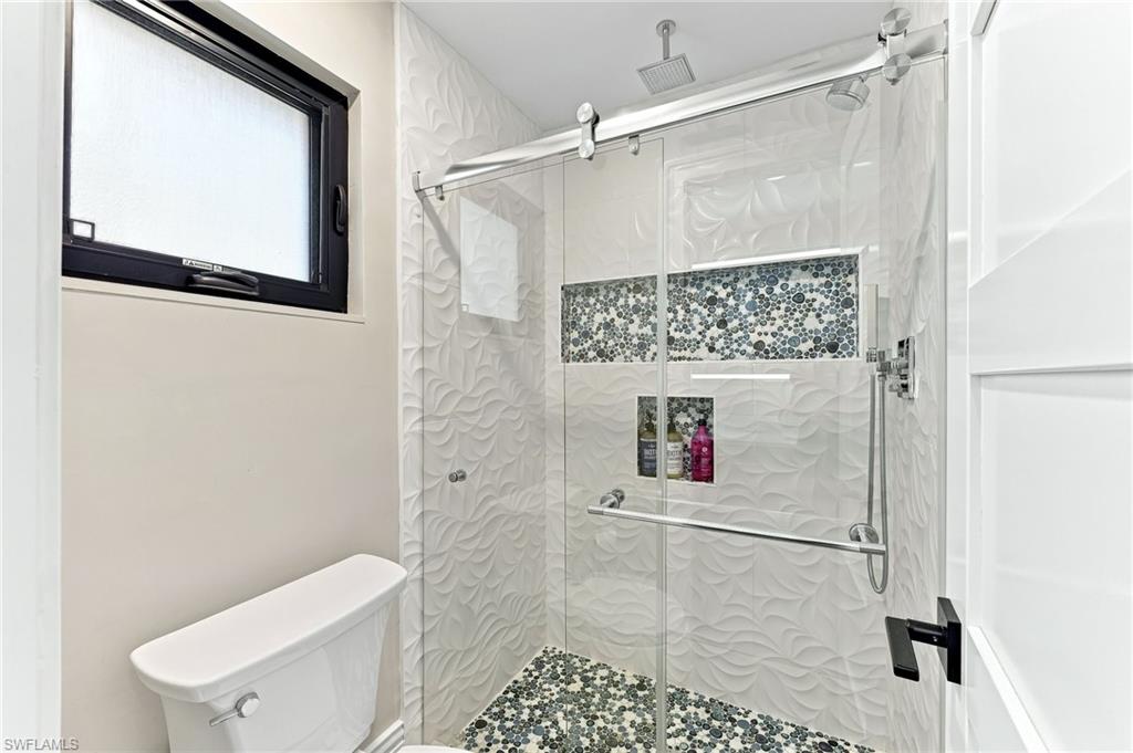 Walk-in shower with textured wall tile and mosaic accent, glass enclosure with sliding door, and integrated shower niches