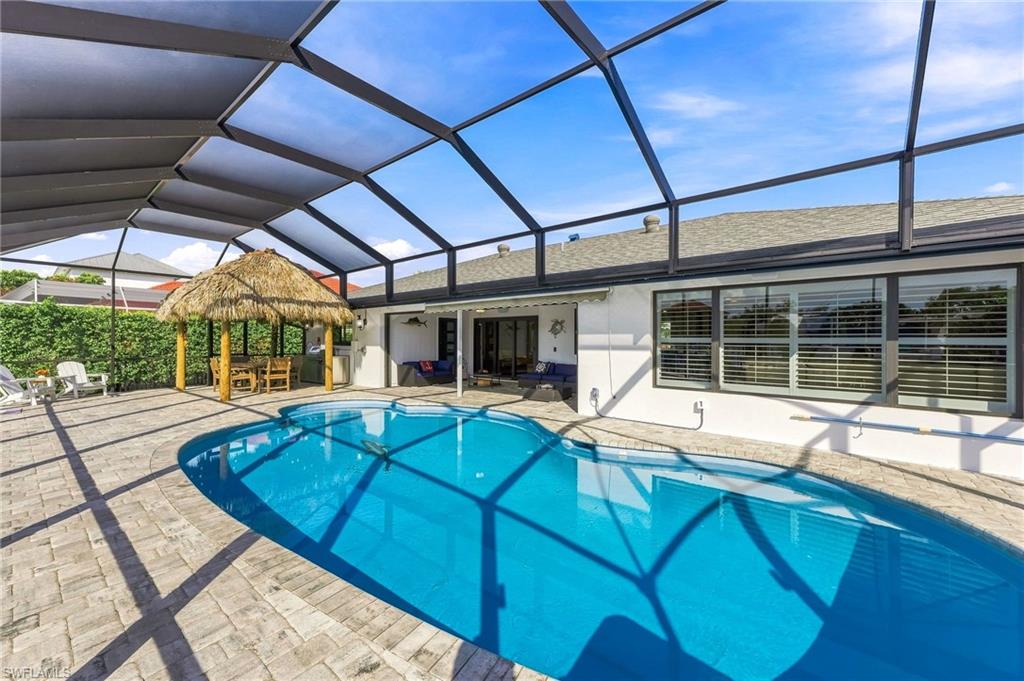 Screened lanai encompassing a freeform swimming pool, paver patio, and a tiki-style hut with seating