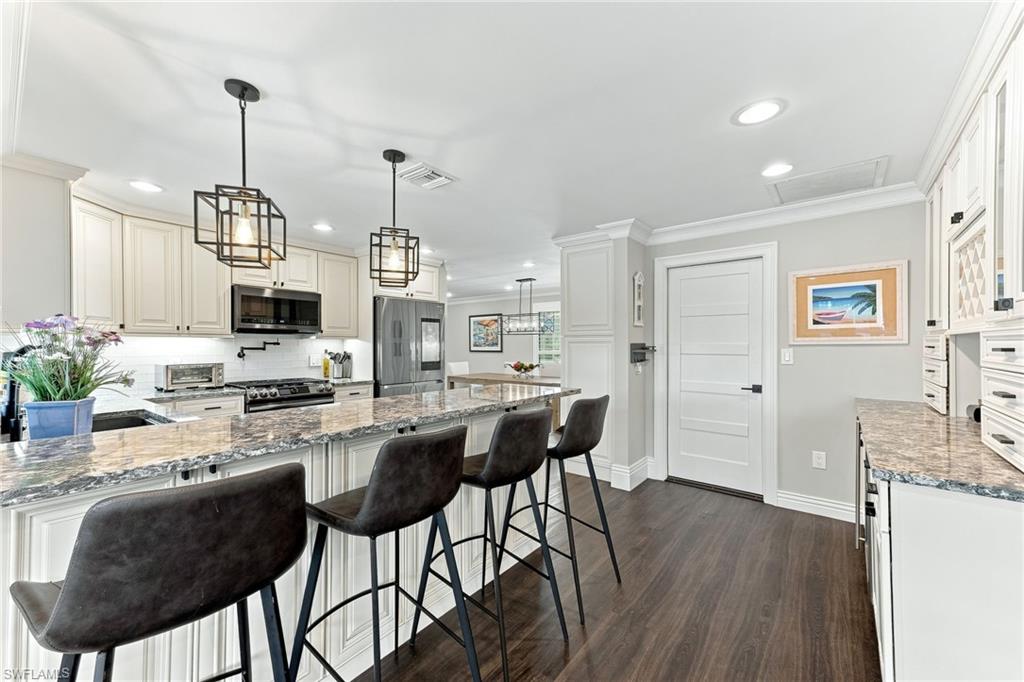 Kitchen featuring a large island with stone countertops, white shaker-style cabinetry, dark wood-finish flooring, recessed lighting, and modern pendant lights