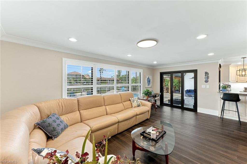 Dark wood-finish flooring, white plantation shutters, crown molding, recessed lighting, and black framed glass doors