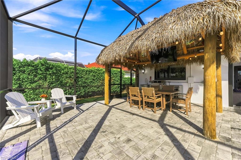 Screened outdoor living area featuring a thatched tiki bar with built-in kitchen, string lighting, and paver flooring