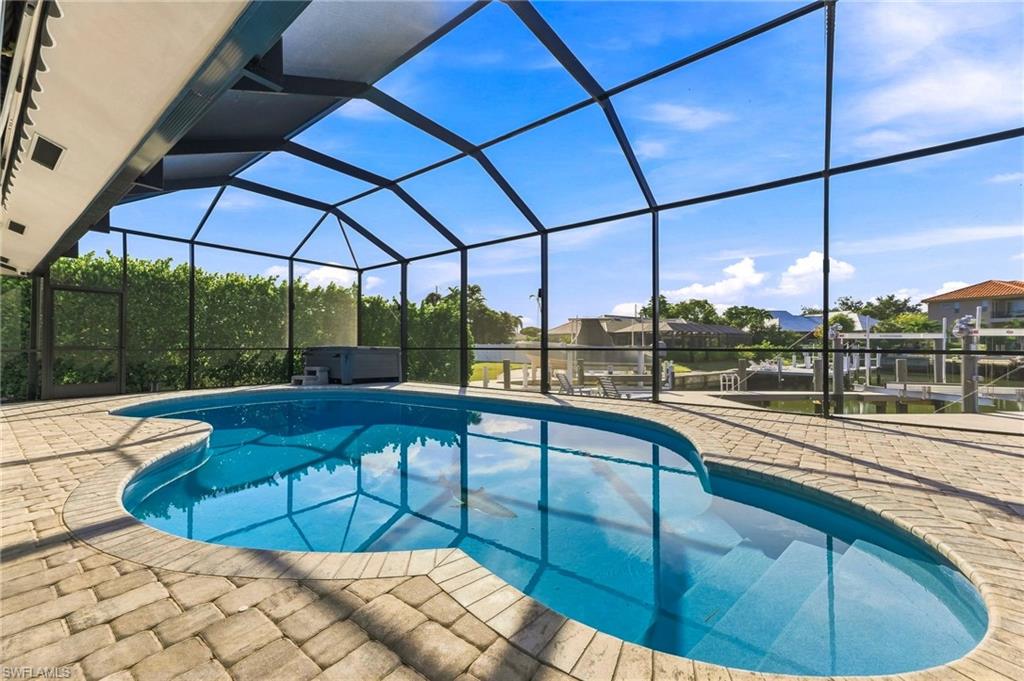 Screened outdoor living area featuring a freeform pool, paved deck, and adjacent spa