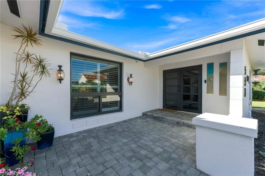Paver patio entryway with a double door entry, featuring dual exterior wall sconces and a prominent fixed window with integrated blinds