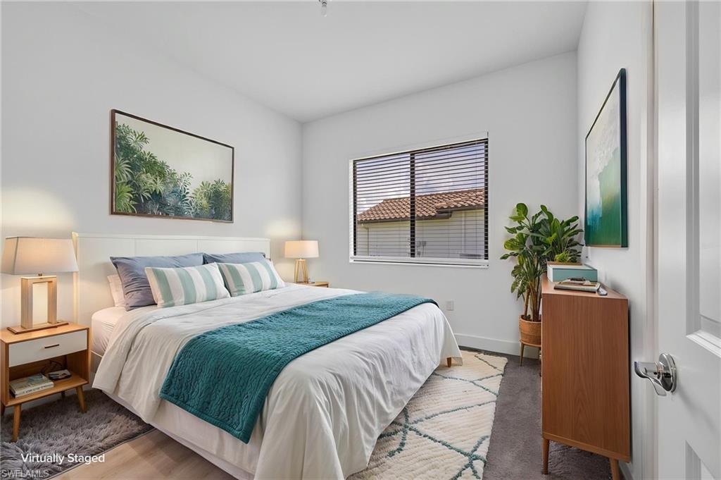 Light wood-finish flooring, white walls, horizontal window blinds, white interior door, and a low-pile carpeted area